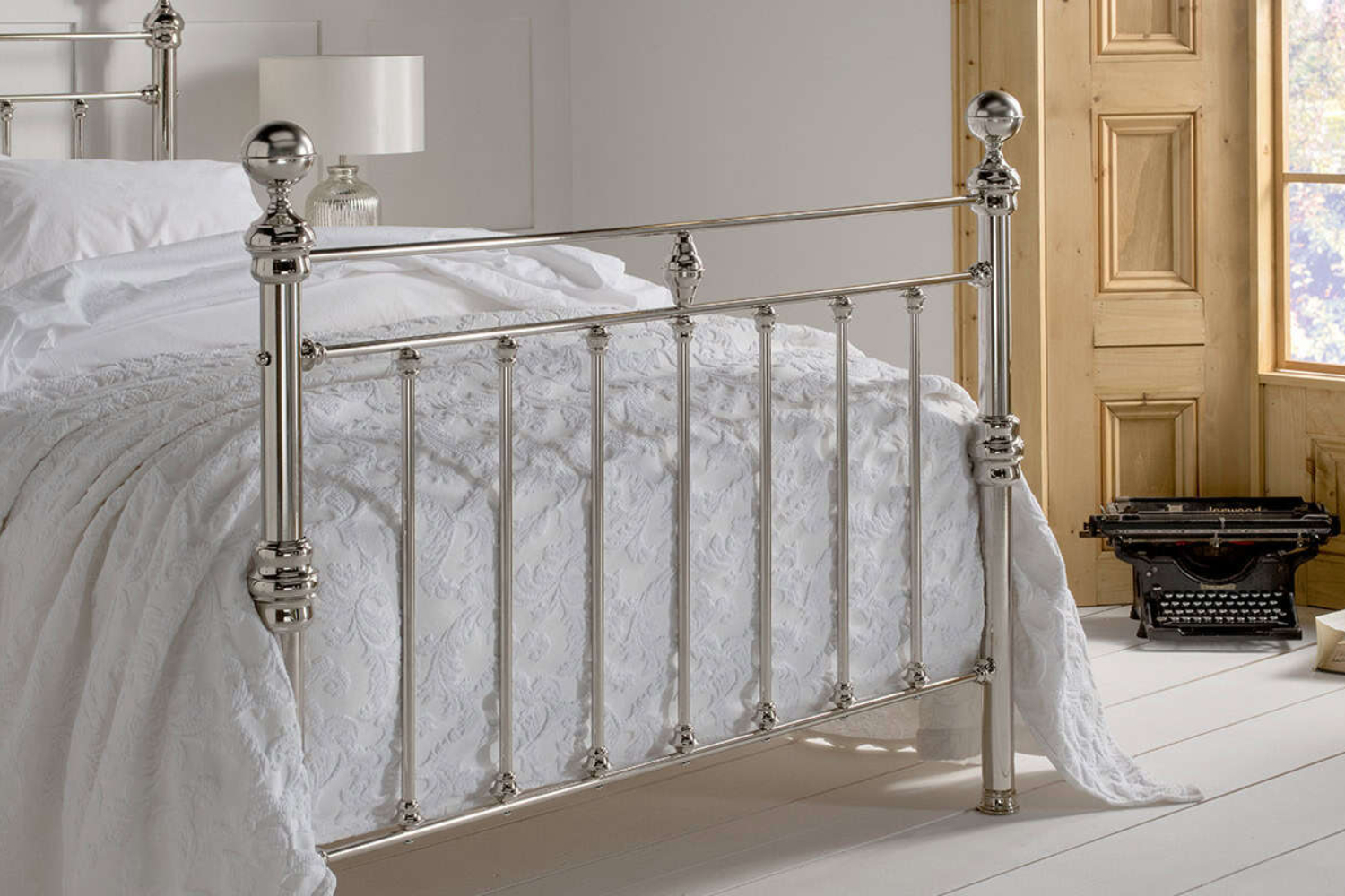 Elegant nickel bed frame with vertical bars and a high footboard, placed in a classic white bedroom setting