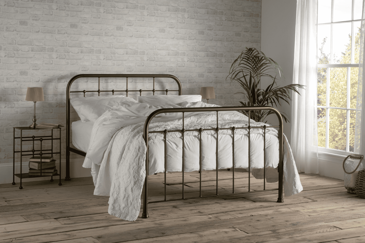 Henry iron bed frame in a warm bronze finish, styled in a cosy brick-wall bedroom with white bedding and wooden floors