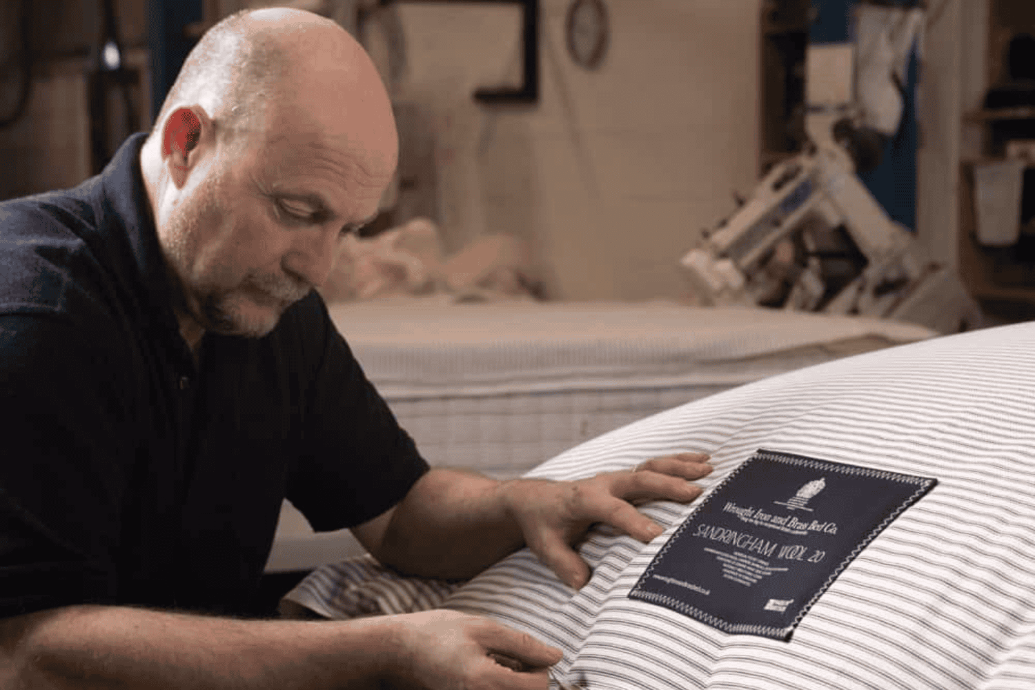 Craftsman hand-finishing a luxury mattress with striped ticking and Royal Warrant label in a workshop setting