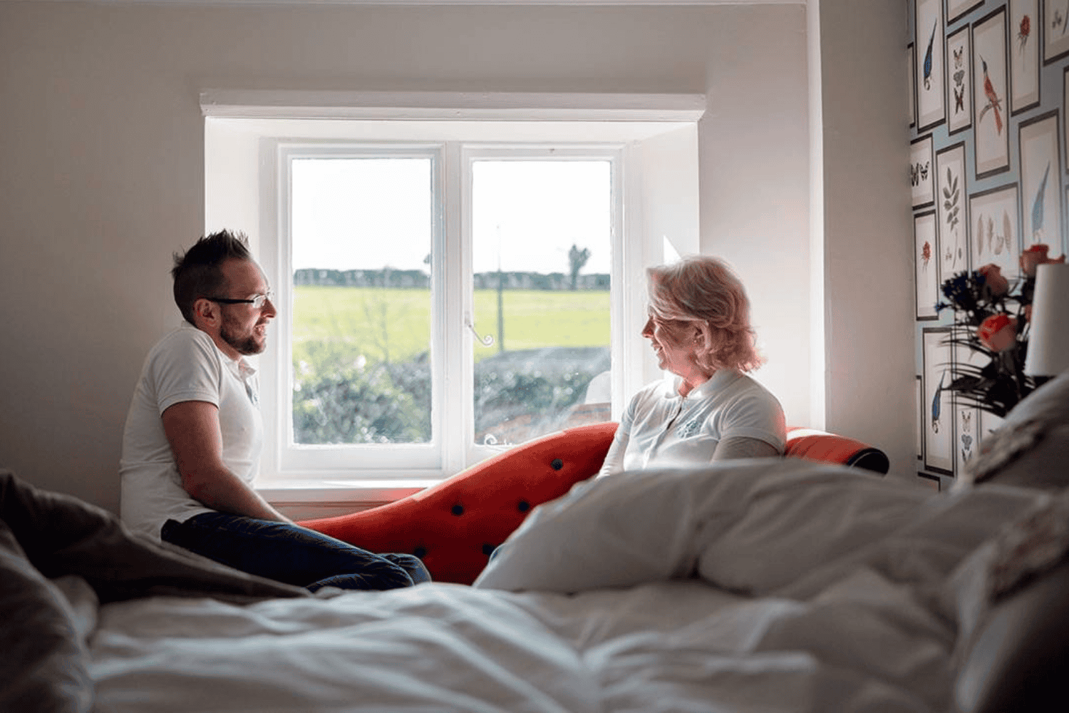 Harry and Amanda sitting on a handmade iron bed, talking by the window in a light-filled bedroom