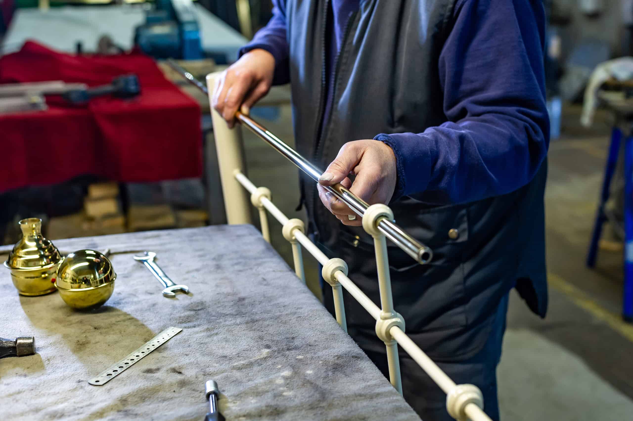 Craftsman assembling and polishing brass components for a handmade bed frame in a workshop.